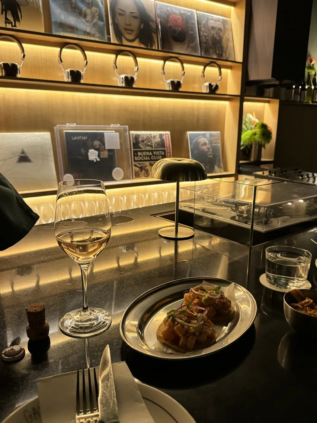 Copa de vino blanco y una tapa emplatada en la barra de Gastón